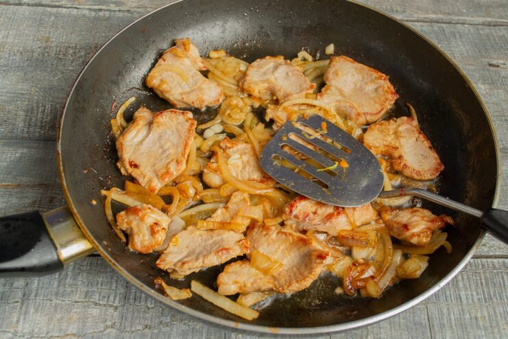 Sautéing Pork with Onions and Garlic Until Soft Pork, onions, and garlic sautéing together in a skillet.