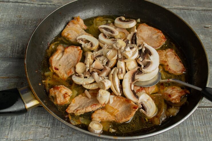 Adding Sliced Mushrooms to the Skillet Thinly sliced button mushrooms being added to the meat and onion mixture in the skillet.