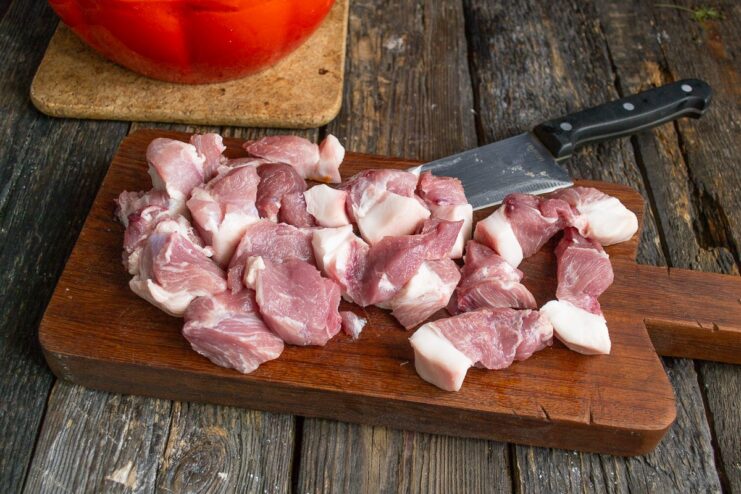 Cutting the Pork into Large Pieces Against the Grain Raw pork being cut into large chunks on a cutting board.