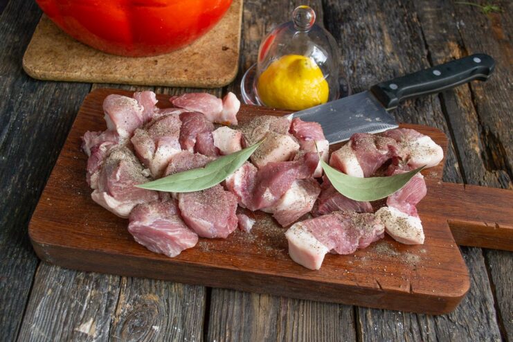 Marinating the Pork with Simple Spices and Lemon Juice Pork pieces in a bowl being mixed with marinade ingredients like pepper and bay leaf.