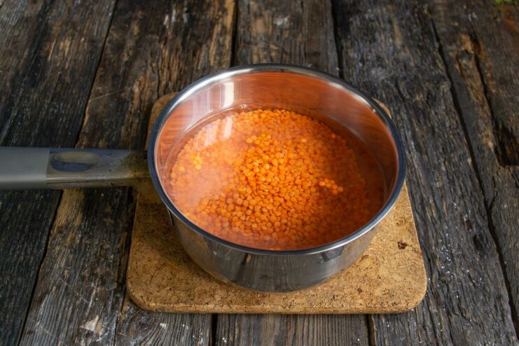 Adding Red Lentils and Water to a Saucepan Dry red lentils in a saucepan with water being added.