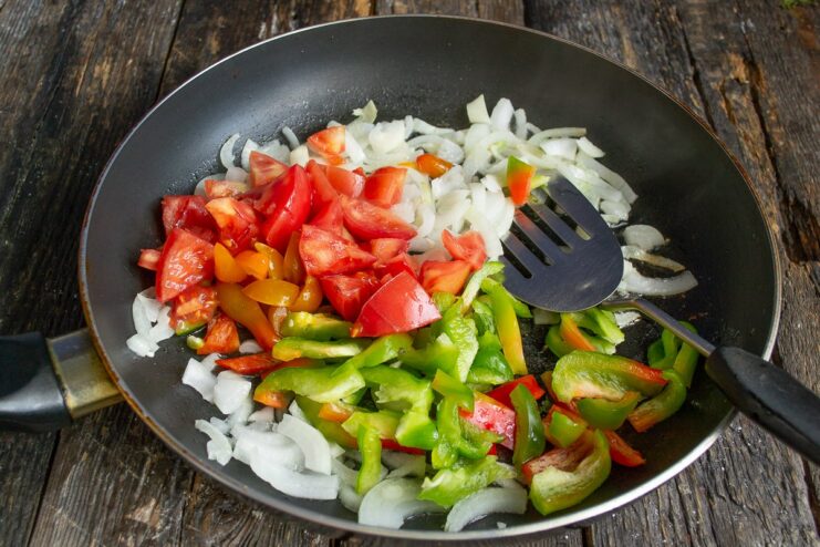 Sautéing the Vegetables Until Softened Chopped onions, tomatoes, and bell peppers being sautéed in a pan.