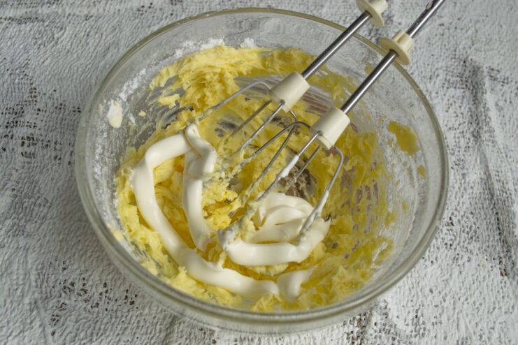 Adding the secret ingredient - mayonnaise - for extra moisture and tenderness in the cookie dough. Adding mayonnaise and vanillin to the creamed butter and egg mixture in a bowl.