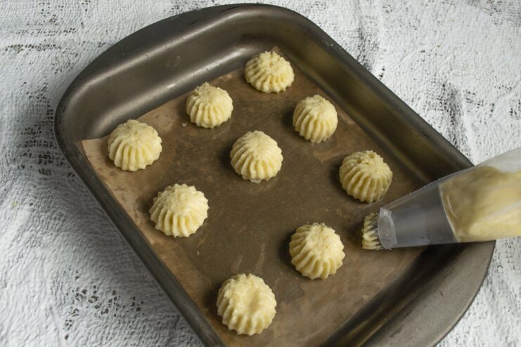 Piping small, uniform cookies onto a baking sheet ensures they bake evenly. Piping small, star-shaped cookies from a piping bag onto a baking sheet lined with parchment paper.