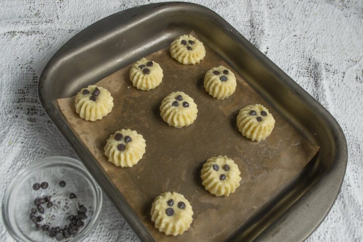 Adding heat-stable chocolate chips ensures they hold their shape while baking. Placing chocolate chips onto the piped raw cookie dough on a baking sheet.