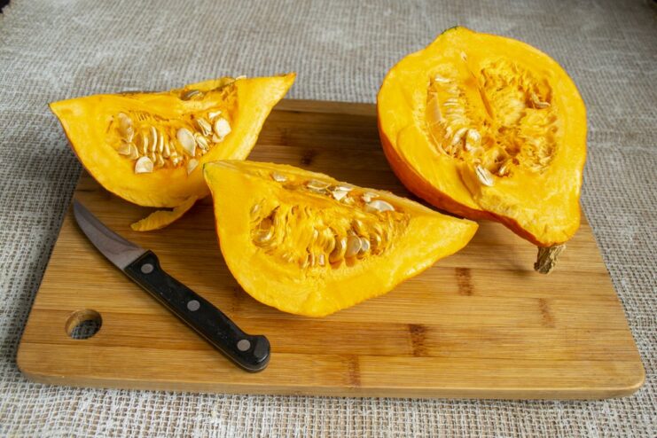 How to prepare pumpkin for purée: peeling and deseeding. Peeled and sliced raw pumpkin pieces on a cutting board.