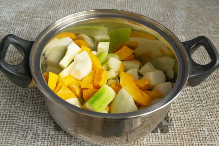 Combining pumpkin, zucchini, and apples in a pot to start cooking. A pot filled with chopped pumpkin, zucchini, and apples with a little water at the bottom.