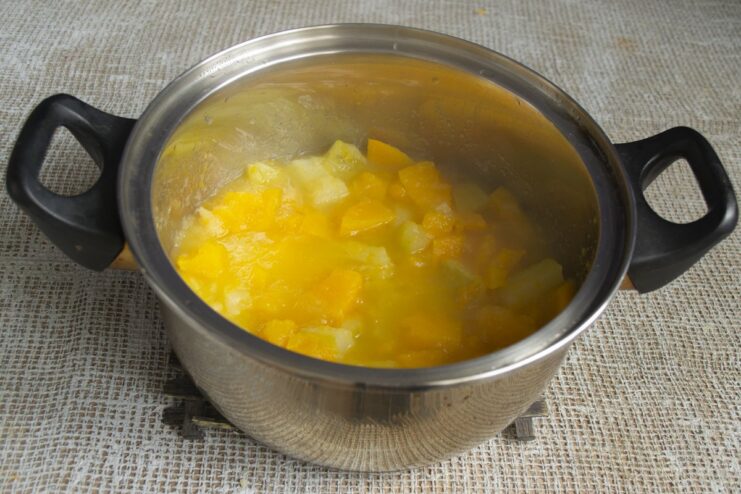 Simmering the vegetables and fruits until they are very soft. Cooked and softened pumpkin, zucchini, and apples simmering in a pot.