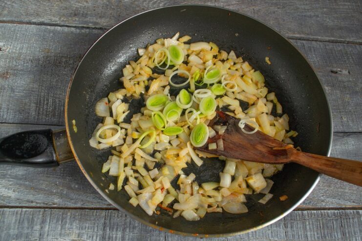 Sautéing Onions and Leeks Until Translucent - The Flavor Base Diced yellow onion and sliced leek being sautéed in a frying pan.