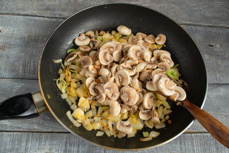 Cooking Mushrooms with Onions - Building Savory Flavor Sliced champignon mushrooms being added to the sautéed onions in a pan.