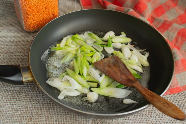 Sautéing chopped green onions in a hot skillet to build the flavor base. Chopped green onions being sautéed in a skillet with oil and butter.