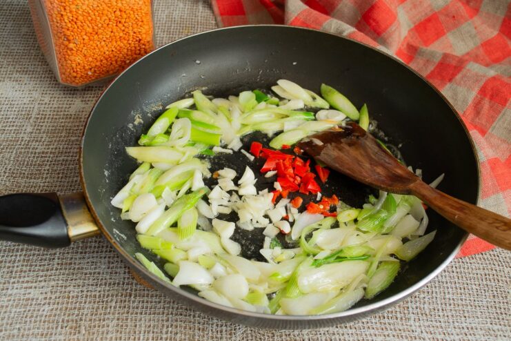 Adding minced garlic and chili to the onions for an aromatic base. Minced garlic and chili peppers being added to sautéed onions in a skillet.