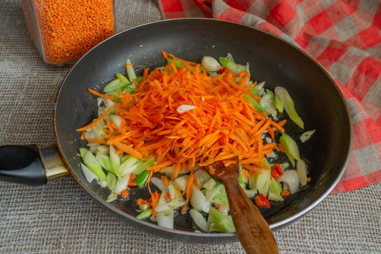 Adding grated carrots to the skillet and cooking until softened. Grated carrots being sautéed with onions, garlic, and chili in a skillet.