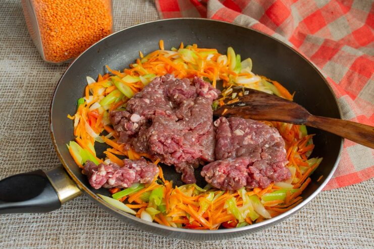 Breaking up the ground beef in the skillet with the vegetables. Ground beef being added to the skillet with sautéed vegetables.