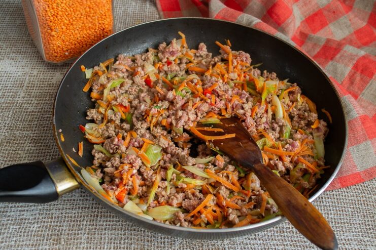 Browning the ground beef with vegetables before adding more ingredients. Ground beef and vegetables being cooked together in a large skillet.