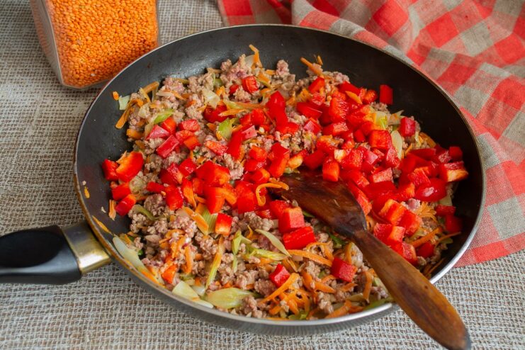 Adding diced bell peppers to the chili con carne mixture. Diced bell peppers being added to the ground beef and vegetable mix in a skillet.