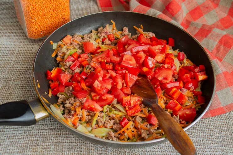 Adding fresh chopped tomatoes to the skillet for a rich sauce. Chopped fresh tomatoes being added to the chili con carne in the skillet.