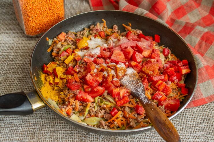Sprinkling turmeric, paprika, and other spices into the chili. A mix of colorful spices being added to the chili con carne in the skillet.