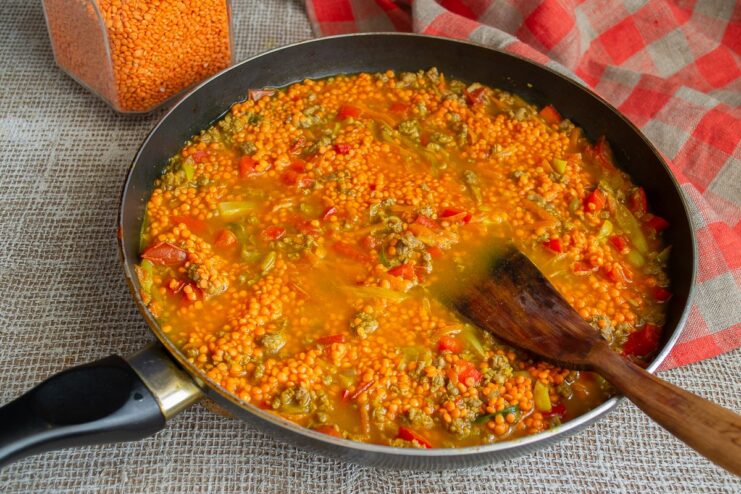 Adding hot broth to the chili and lentils before simmering again. Hot liquid being poured into the skillet with chili con carne and lentils.