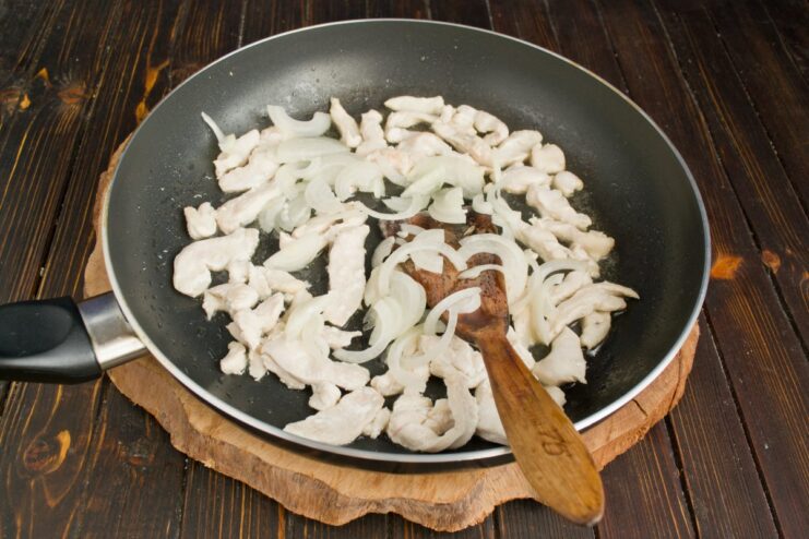 Adding Sliced Onions to the Sautéed Chicken Sliced onions being added to the pan with sautéed chicken strips.