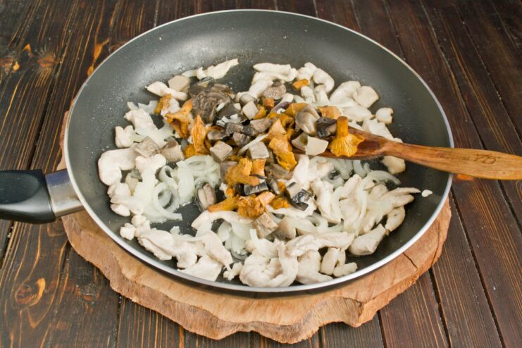 Incorporating Cooked Mushrooms into the Sauce Cooked, chopped mushrooms being added to the chicken and onions in the pan.