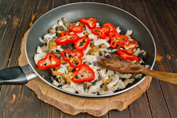 Adding Sliced Bell Peppers for Flavor and Color Sliced red bell pepper rings being added to the pan with chicken, onions, and mushrooms.