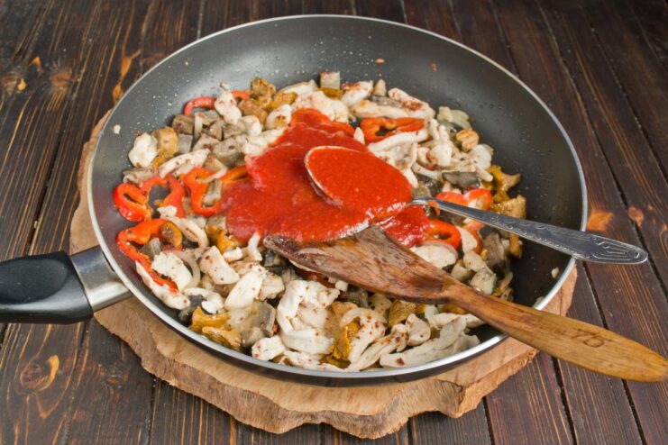 Simmering the Sauce with Tomato, Salt, and Pepper Tomato sauce being poured into the frying pan with vegetables and chicken to create the pasta sauce.