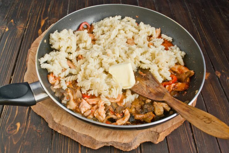 Combining Cooked Pasta with the Chicken and Mushroom Sauce Cooked pasta being mixed with the chicken, mushroom, and tomato sauce in a large pan.