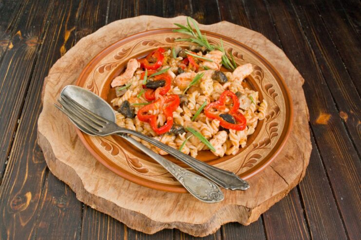 Garnishing the Pasta with Cheese and Fresh Herbs Before Serving A finished plate of chicken and mushroom pasta being garnished with grated cheese and fresh green herbs.