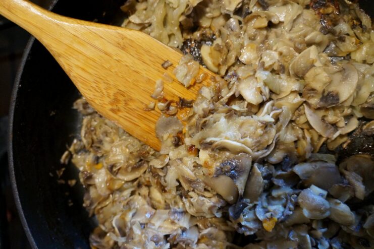 Mushrooms and onions being sautéed in a black frying pan.