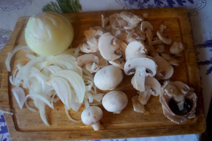 Sliced onions and chopped champignons on a cutting board, ready for cooking.