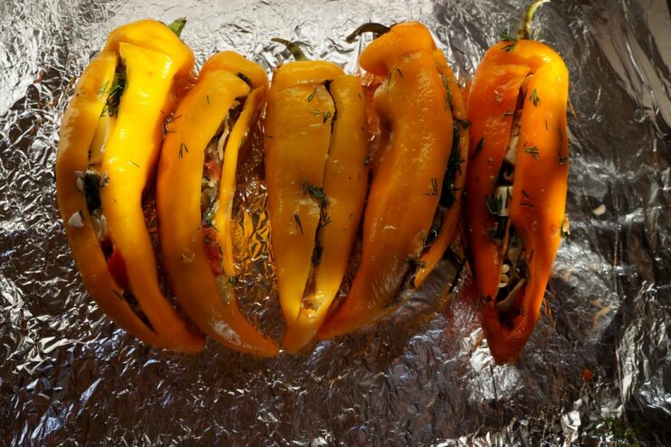 Red peppers on a foil-lined baking sheet, being filled with the mushroom and feta mixture.