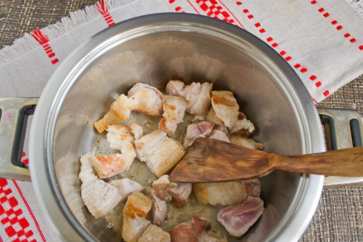 Searing pork belly pieces until golden brown for the pilaf base Pieces of pork belly being sautéed until golden in a heavy-bottomed pot.