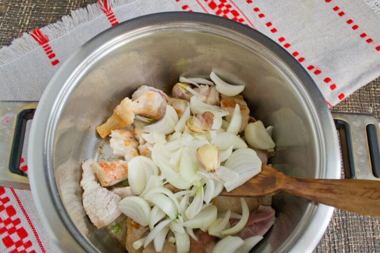 Adding chopped onion and garlic to the seared pork Chopped onion and crushed garlic being added to the pot with seared pork.
