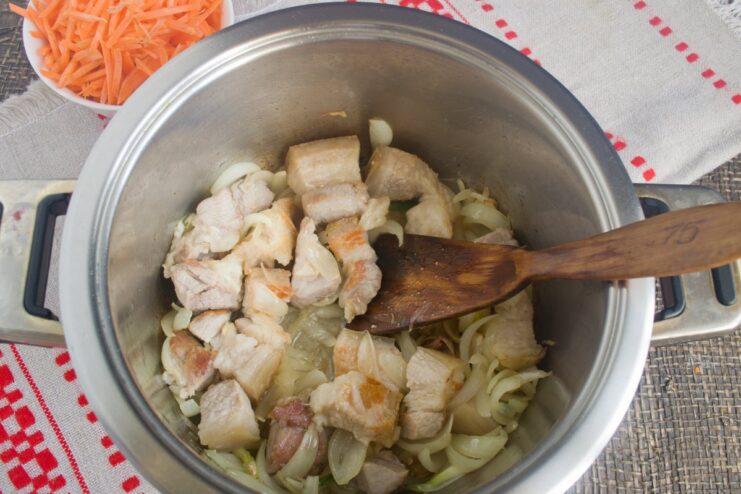 Cooking pork with aromatics until the onion is caramelized Pork belly, onion, and garlic being sautéed together in a pot.