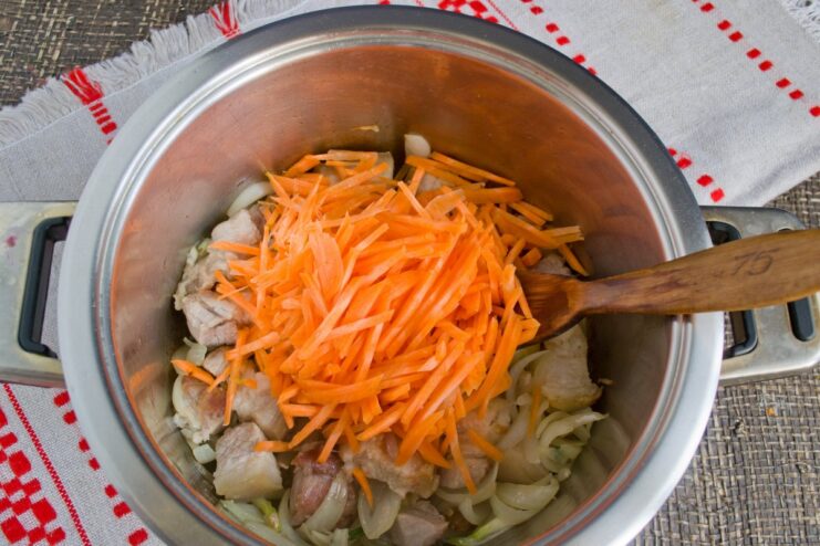 Adding carrots to the pork and onion mixture to build flavor Julienned carrots being added to the pot with pork, onion, and garlic.