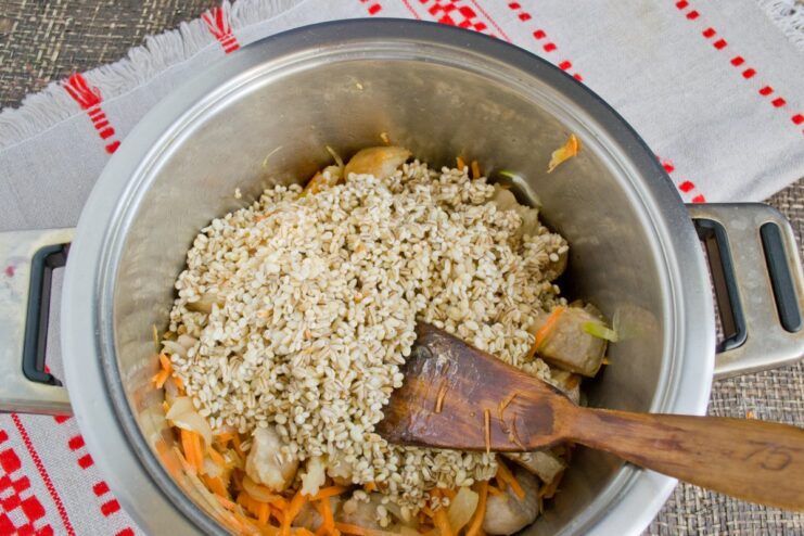 Adding rinsed pearl barley to the pot with meat and vegetables Rinsed pearl barley being added on top of the meat and vegetables in the pot.