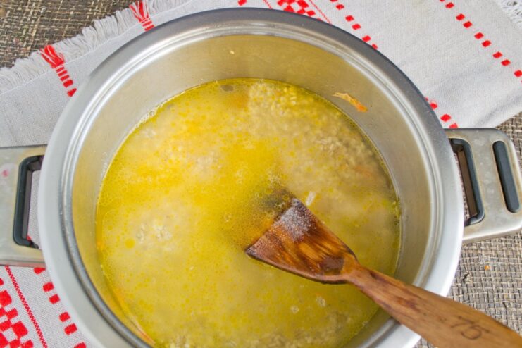 Pouring water over the pearl barley and meat to start the simmering process Cold water being poured into the pot covering the pearl barley and meat.