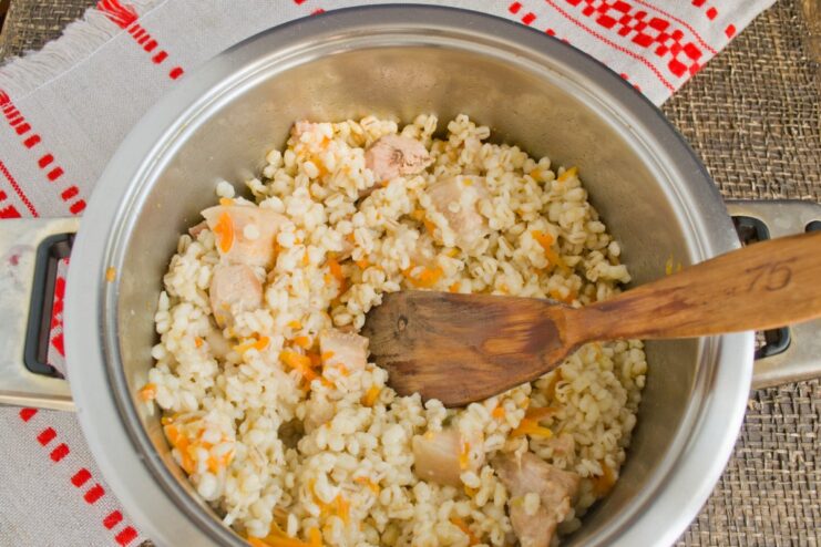 Simmering the pearl barley pilaf slowly to cook the grains perfectly The pot with pearl barley and meat simmering on the stove.