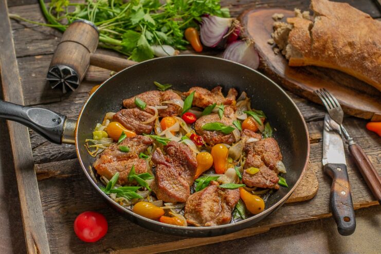 A plate of spicy fried pork with caramelized onions and whole cherry tomatoes, garnished with green onions.