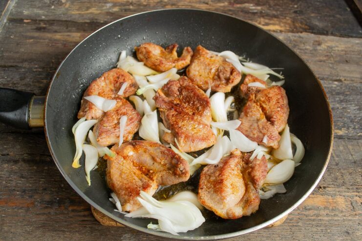 Step 5: Adding and Caramelizing the Onions Sliced onions added to the pan with golden-brown pork cutlets.