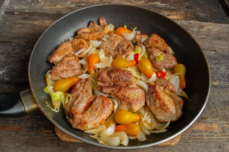 Step 6: Adding Chili and Cherry Tomatoes Chili rings and whole cherry tomatoes being cooked with pork and onions in a pan.