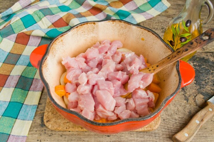 Adding Pork to the Pot: The Next Step in Making Plov Pieces of chopped pork being added to the pot with fried carrots and onions.