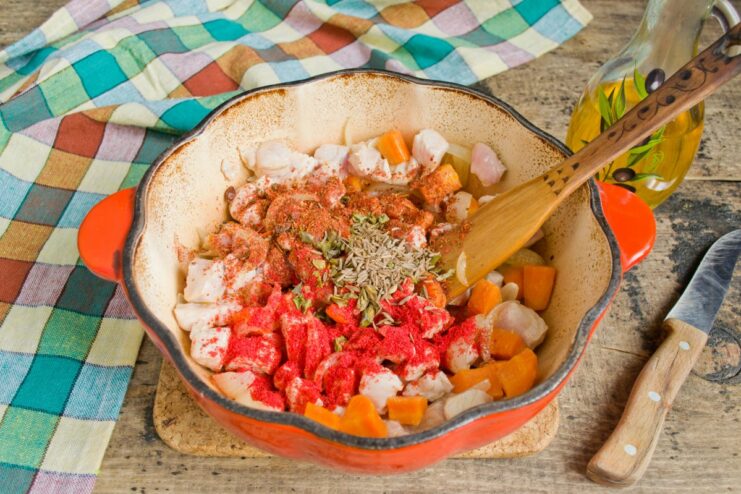Seasoning the Plov: Adding Spices for an Aromatic Dish A hand sprinkling spices like paprika and cumin over the meat and vegetables in the pot.