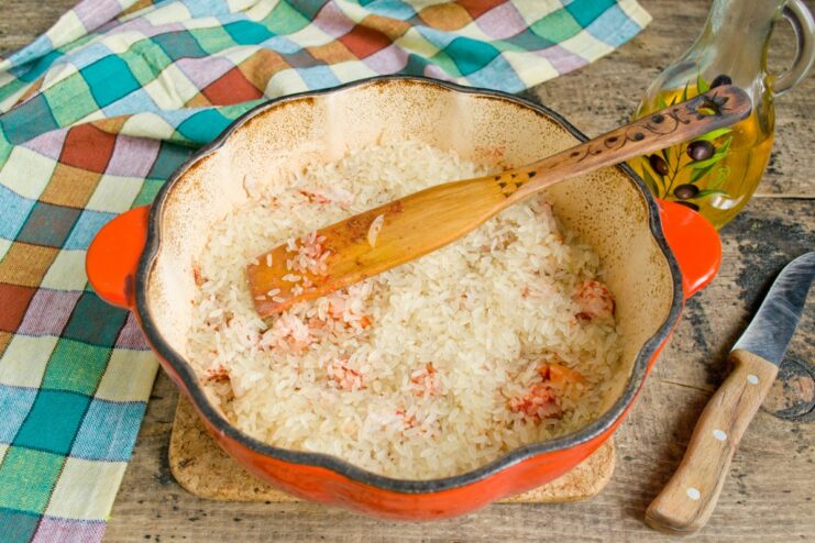 Adding Rice to the Plov: Layering the Ingredients Parboiled long-grain rice being poured over the meat and vegetables in the pot.
