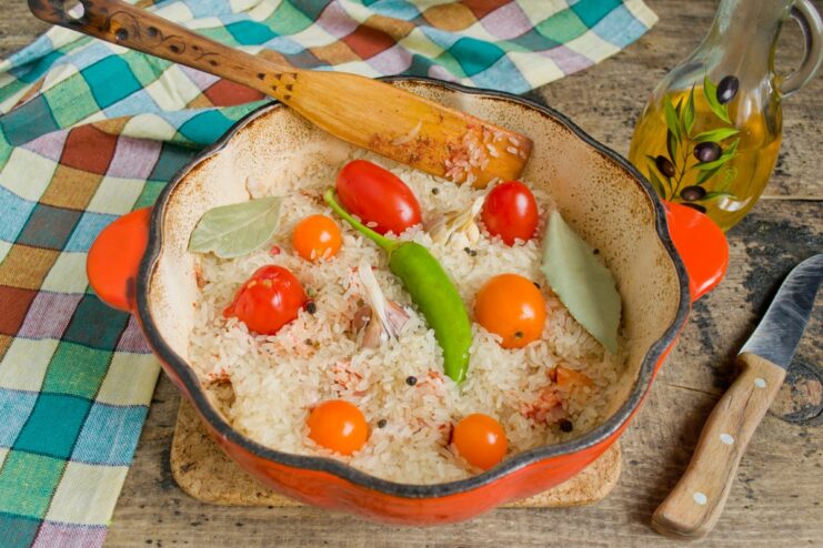 Adding Aromatics: Garlic, Chili, and Tomatoes for Extra Flavor Whole garlic heads, a chili pepper, and cherry tomatoes placed on top of the rice in the pot.