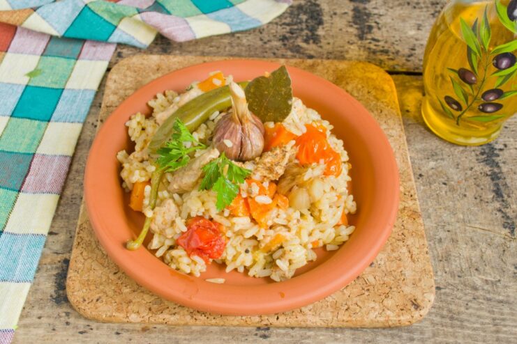 Serving the Plov: A Hot and Hearty Meal Ready to Enjoy A serving of hot plov with meat on a plate, garnished with fresh herbs and a garlic head.