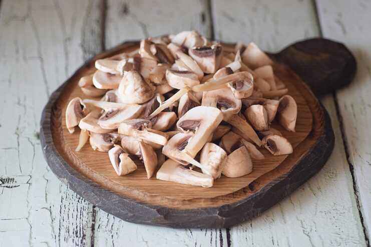 Slicing Mushrooms - Cut the mushrooms into thick slices to retain their flavor and texture. A person's hands slicing fresh champignon mushrooms on a cutting board.