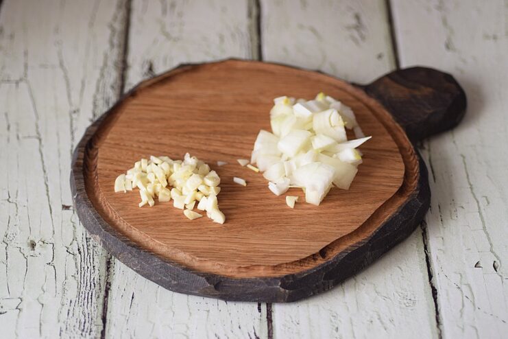 Mincing Onion and Garlic - Finely chop the aromatics to build the flavor base. Finely chopped onion and garlic on a cutting board, ready to be added to the pan.
