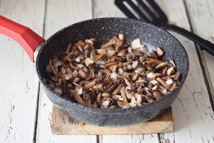 Adding Aromatics - Add the minced onion and garlic to the golden-brown mushrooms. Adding minced onion and garlic to the pan with sautéed mushrooms.